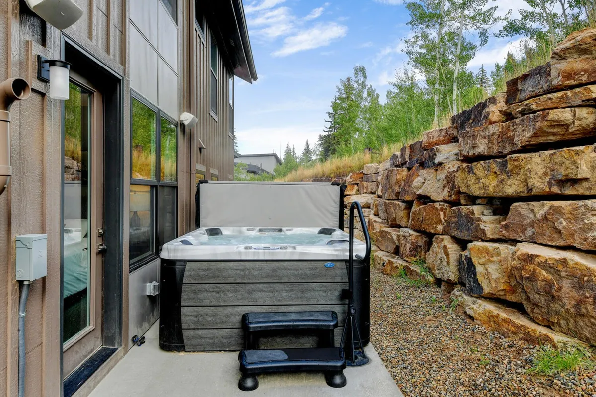 This exterior image captures a private hot tub nestled against a rock wall, surrounded by lush greenery. The tranquil scene suggests both relaxation and a strong connection to the surrounding Colorado landscape, with hints of sunset or early morning light.