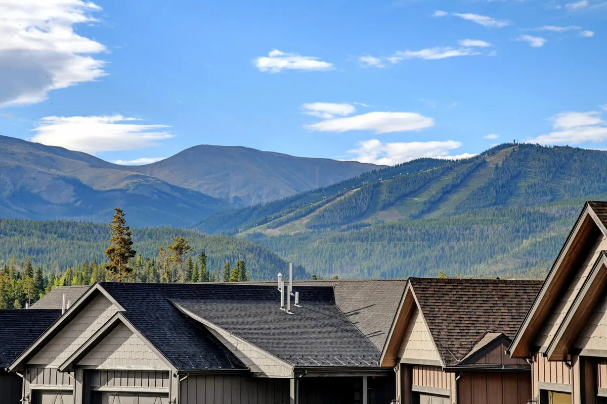 An exterior view featuring rooftops nestled below towering mountains beneath an expansive, tranquil sky. The image hints at nearby nature trails and the vast outdoor experiences available in both summer and winter.