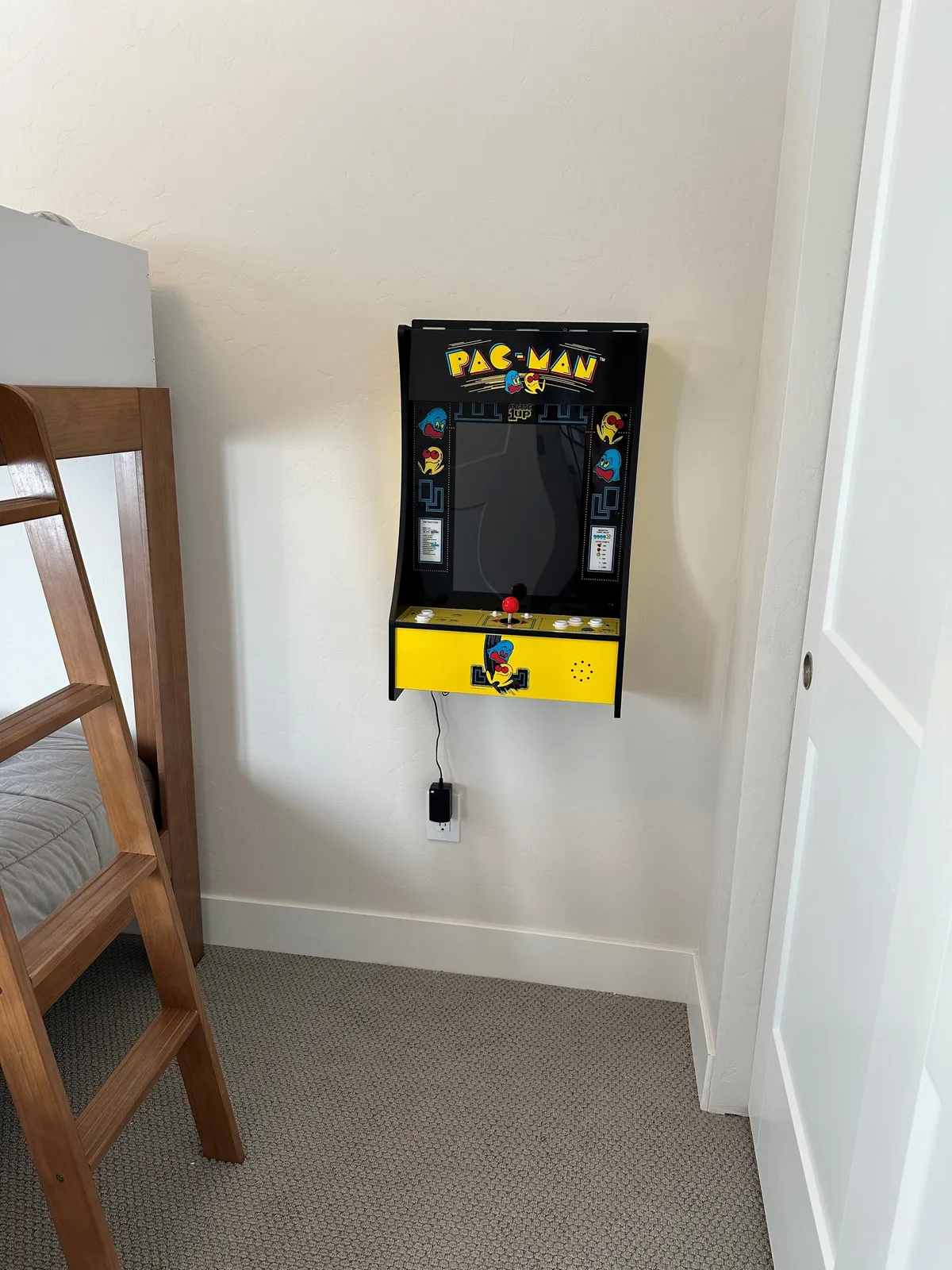 A vibrant interior scene featuring a Pac-Man arcade machine next to a wooden ladder and bed frame. The space has an inviting, nostalgic feel, encouraging guests to gather and enjoy classic games together. The setting suggests a playful atmosphere perfect for family fun and friendly competition.