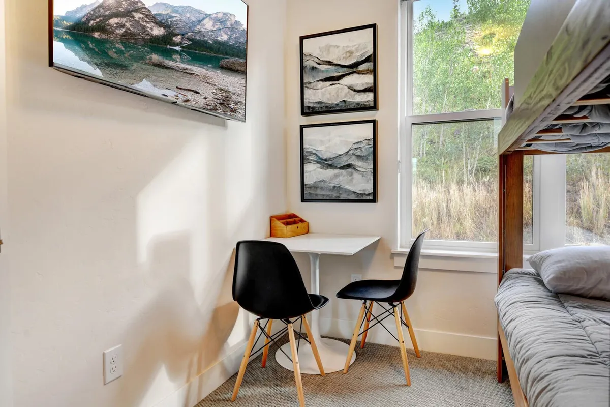 This interior image focuses on a creative family space with a double bunk bed, a dining table and chairs, playful wall art, a television, and a window with a scenic view. The area feels comfortable and playful, ideal for children and family bonding.