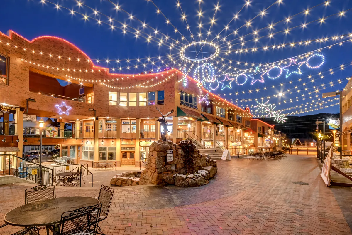 A lively exterior scene with twinkling lights, decorative stars, a stone fountain, and seating areas—evoking the festive atmosphere of downtown Winter Park’s shops, dining, and events.