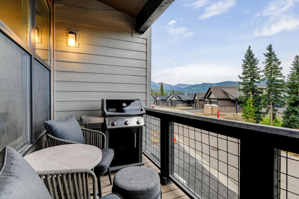 An exterior deck scene with comfortable balcony seating, a grill, and a stunning mountain vista. The relaxed atmosphere encourages outdoor dining, socializing, and enjoying sunset views over the mountains.