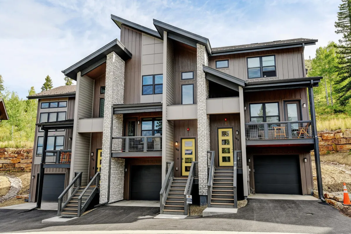 A modern chalet exterior is showcased, featuring sleek stone accents, bold yellow front doors, and spacious balconies. The design hints at high-end finishes and spaces ideal for gatherings, with an inviting, contemporary mood.