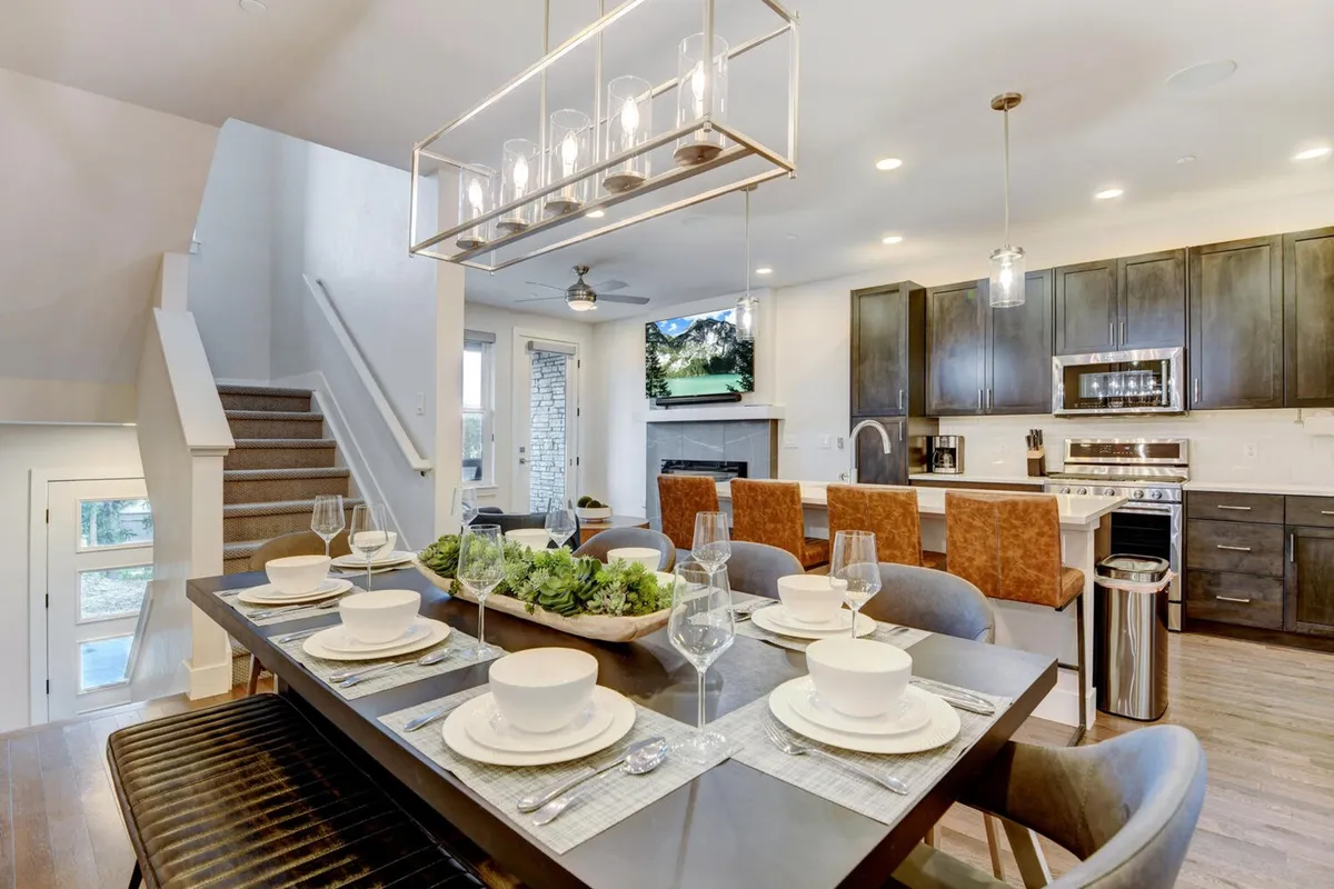 The image shows a stylish, sunlit dining area set for a meal, with a modern kitchen in the background and a sliding glass door that opens to an inviting outdoor space. The elegant table is ready for family gatherings or festive celebrations, creating a warm and welcoming atmosphere.
